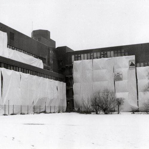 Das Bild zeigt das verhüllte Gebäude A 1-4. Auch das im Text erwähnte Plakat ist zu erkennen. Um das Gebäude herum liegt Schnee.