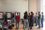 The photo shows the members of the network from behind, standing in front of a row of flipcharts covered with posters. They listen as three colleagues present something on a flipchart.