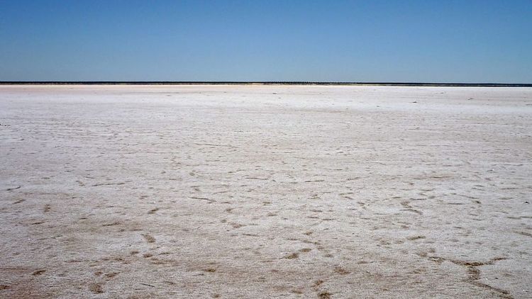 Landschaftsbild: Glatter, weißer Untergrund (das Salz), darüber blauer Himmel, im Hintergrund ein dünner, dunklerer Streifen am Horizont.