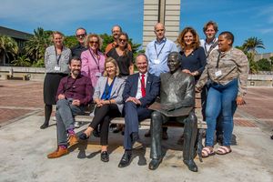 Delegationsbesuch an der NMU Eine Gruppe von Personen posiert vor der Büste von Nelson Mandela. Im Hintergrund Gebäude und Palmen.