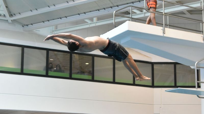 Ein Student macht einen gestreckten Salto rückwärts vom Dreimeterturm.