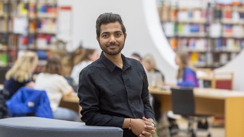 Junger Mann vor dem Hintergrund des großen Saals im Erdgeschoss der Unibibliothek.                                        -Bibliothek.