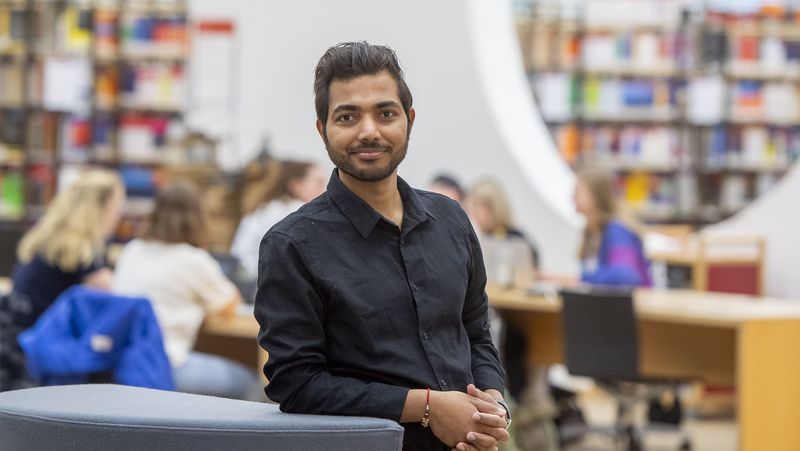 Junger Mann vor dem Hintergrund des großen Saals im Erdgeschoss der Unibibliothek.                                        -Bibliothek.