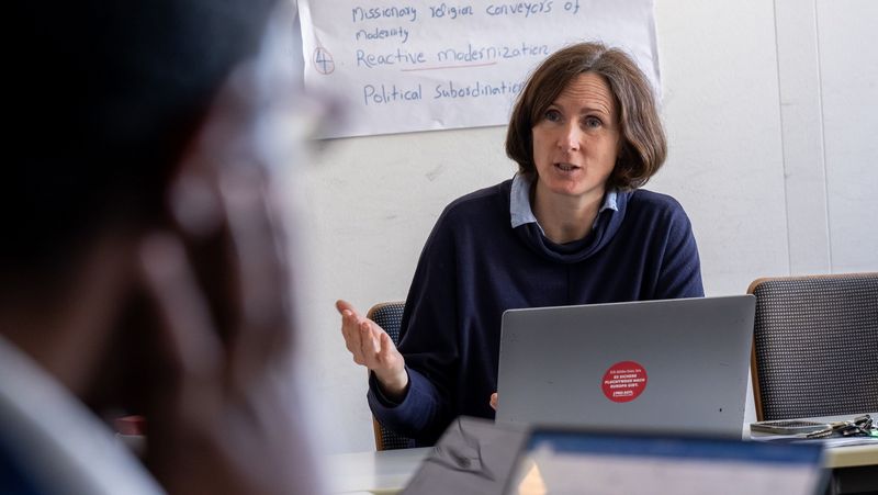 Das Bild zeigt Malve von Möllendorf. Sie sitzt hinter einem Laptop und erklärt einem Teilnehmendem des Kolloquiums einen Sachverhalt.