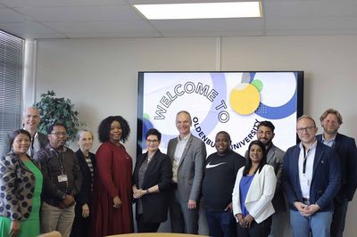 Gruppenbild Eine Gruppe von zwölf Personen posiert vor einem Schild mit dem Text "WELCOME TO OLDENBURG UNIVERSITY".