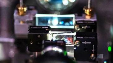 Das Bild zeigt einen komplizierten Versuchsaufbau für ein optisches Experiment. Das Laserlicht durchquert zwei Anordnungen aus jeweils zwei eng hintereinanderliegenden keilförmigen Glasplatten.