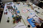 Das Foto zeigt einen Tisch von oben. AUf dem Tisch sind Lego- Steine für das Lego Serious Play ausgelegt, dazu ausgeschnittene Denk- und Sprechblasen sowie Büromaterial 