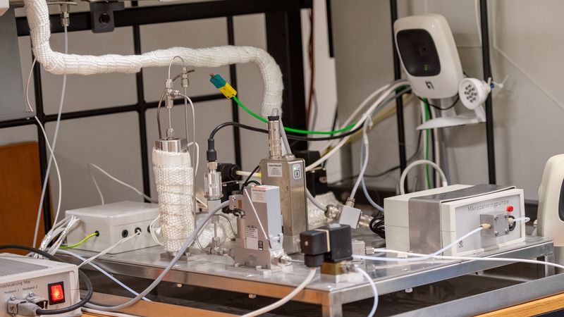 Auf einer Platte befinden sich mehrere metallische Module, die durch Kabel, Schläuche und kleine Röhrchen verbunden sind.