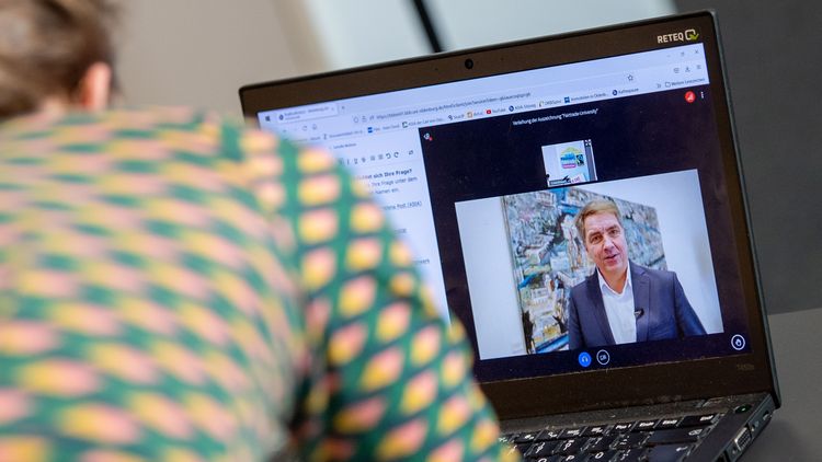 Videobotschaft von Krogmann ist auf einem Laptop-Bildschirm zu sehen, im Vordergrund der Rücken einer Frau.