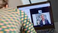 Video message from Krogmann can be seen on a laptop screen, with a woman's back in the foreground. 