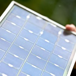 Oblique view of a photovoltaic module, perhaps 30 by 60 centimeters in size, held in the hand of a person.