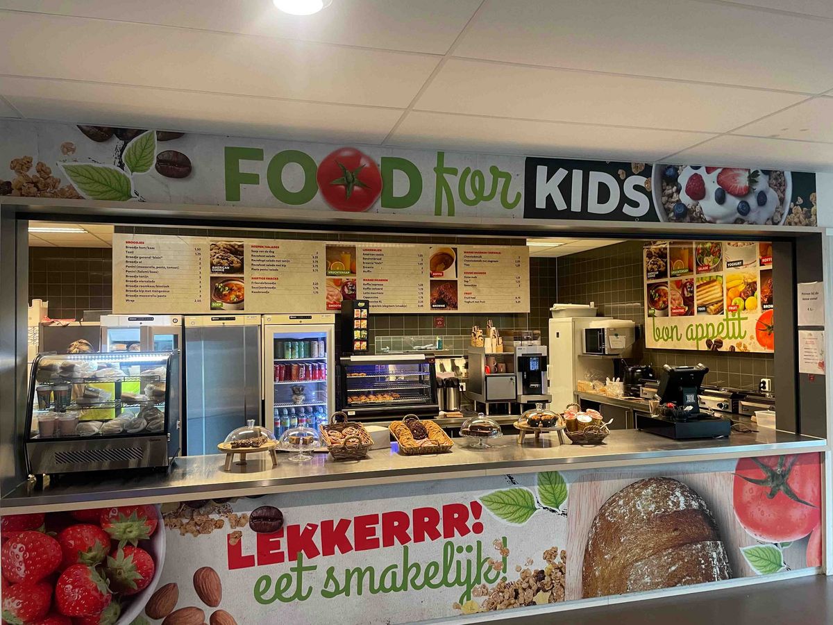 Teaching Across Borders Eine Cafeteria in der Schule Stad&Esch mit einer Speisekarte "FOOD for KIDS" und Lebensmitteln. Auf einem Schild steht "LEKKERRR! eet smakelijk!".
