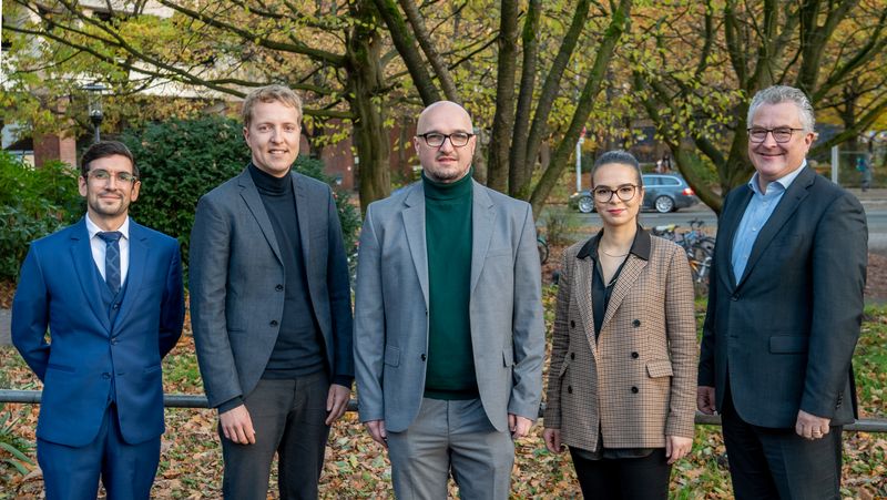 Festlich gekleidete Preisträger in herbstlicher Umgebung.