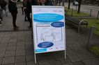 Auf dem Bild ist ein Aufsteller zu sehen, der im Freien steht. Im Aufsteller befindet sich ein Plakat, das auf den Tag des Lehrens und Lernens hinweist. Das Plakat ist mit blauen Elipsen und einem Comic gestaltet.