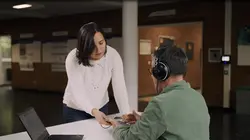 Eine Frau gibt einem Mann, der Kopfhörer trägt, ein Handy in die Hand, um mit ihm einen Hörtest zu machen. 