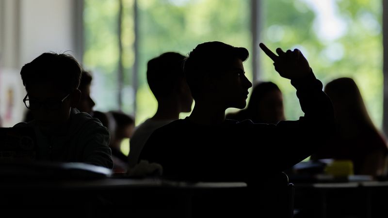 Die Silhouetten von Jugendlichen im Klassenzimmer - ein Schüler meldet sich.