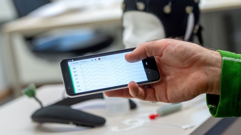 Auf einem Smartphone-Display sind wellenförmige EEG-Messdaten zu sehen.