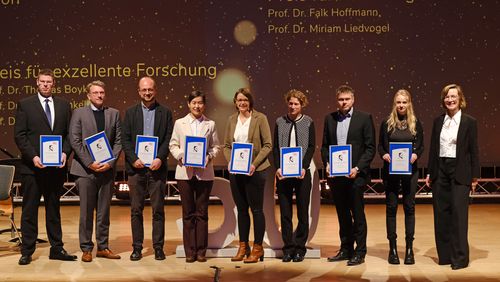 Die Personen stehen nebeneinander auf der Bühne mit ihrer Urkunde in der Hand. 