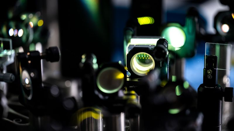 Das Foto zeigt einen Versuchsaufbau. Ein grüner Laserstrahl durchquert mehrere hintereinanderliegende optische Bauteile. 