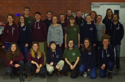 Das Foto zeigt den Fachschaftsrat Umweltwissenschaften für Winter- & Sommersemester 2019/20. Zu sehen sind 21 Studierende, alle im Alter von Anfang bis Ende 20. Sie tragen alle bunte Pullover , Jacken oder T-Shirts mit dem Logo der Fachschaft.  Sie stehen und knien in 3 Reihen. Das Foto wurde im ICBM aufgenommen. Im Hintergrund ist eine Backsteinmauer, links befindet sich ein Modell-Schiff in einer Vitrine, rechts ist die Tür zu einem Labor.