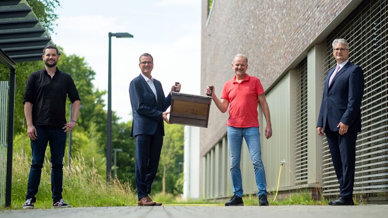 Die vier Herren stehen nebeneinander vor dem Gebäude NeSSy, Herr Edeling und Herr Bartner halten gemeinsam einen Nistkasten.