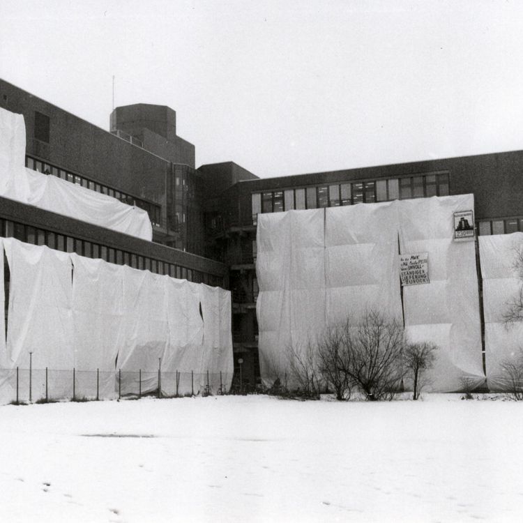 Das Bild zeigt das verhüllte Gebäude A 1-4. Auch das im Text erwähnte Plakat ist zu erkennen. Um das Gebäude herum liegt Schnee.