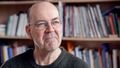 The picture shows Dietmar von Reeken. He is sitting in front of a bookshelf and looking thoughtfully out of the window.