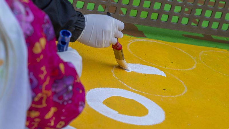 Großaufnahme einer Hand mit Pinsel, der gerade einen weißen Strich auch die gelbe Platte malt