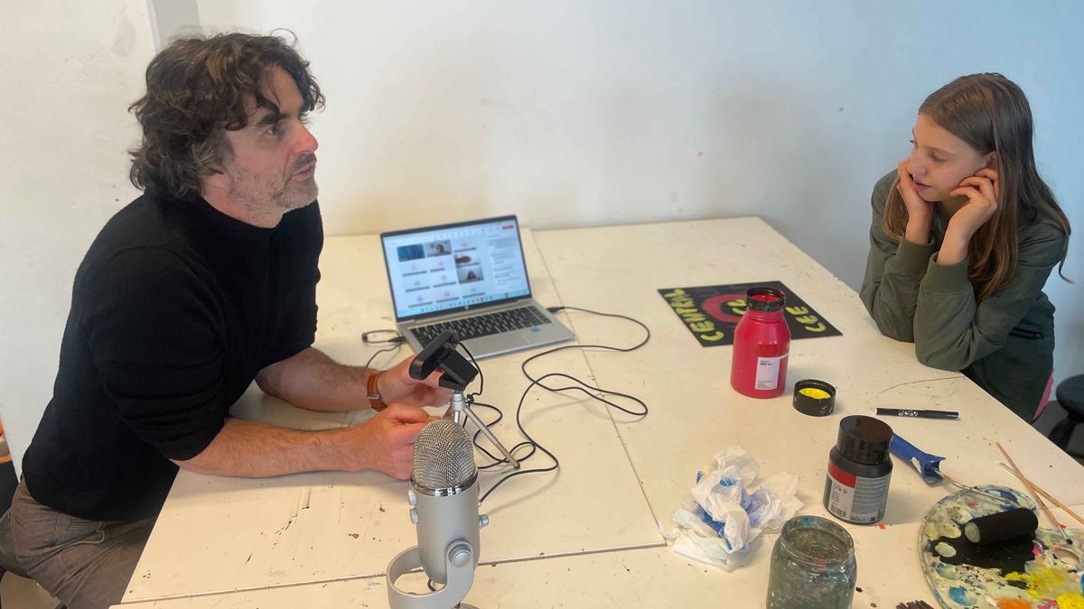 Teaching Across Borders Ein Mann und ein Mädchen sitzen an einem Tisch und arbeiten. Der Mann spricht in ein Mikrofon, das Mädchen ist nachdenklich.