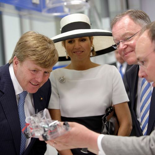 Das Bild zeigt den niederländischen König Willem-Alexander, seine Ehefrau Máxima und den niedersächsischen Ministerpräsidenten Stephan Weil. Sie beugen sich leicht nach vorne zu einem Modell eines Autos mit alternativem Antrieb, das ihnen gerade erklärt wird.