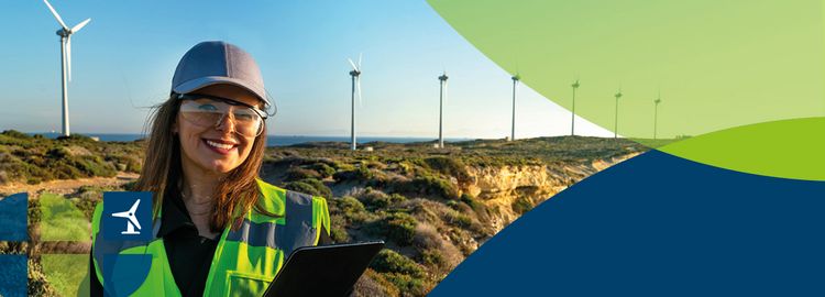 Eine Frau in Warnweste steht vor mehreren Windrädern und lächelt in die Kamera.
