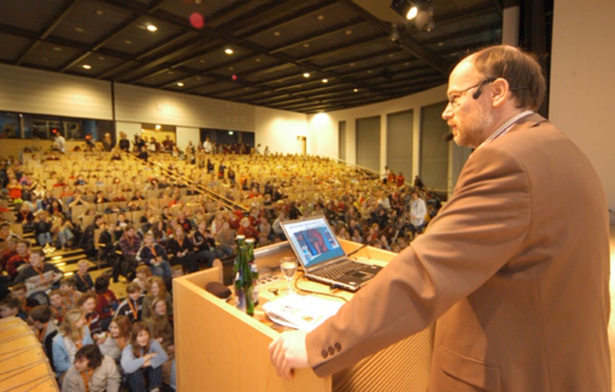 Das Bild zeigt Prof. Dr. Dr. Birger Kollmeier im Audimax bei seiner Vorlesung. Im Auditorium sitzen hunderte wissbegierige Kinder und lauschen seinen Ausführungen.