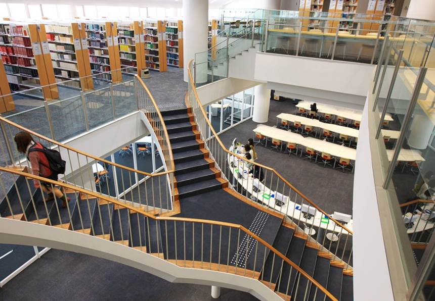 Bibliothek Eine Bibliothek mit hohen Bücherregalen, einer Treppe und Sitzplätzen.