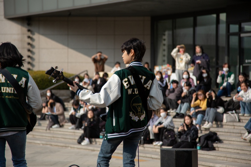 Ewha Womans University Clubs Zwei Personen spielen Gitarre/Bass vor einer Gruppe von Studierenden auf dem Campus der Ewha Womans University.