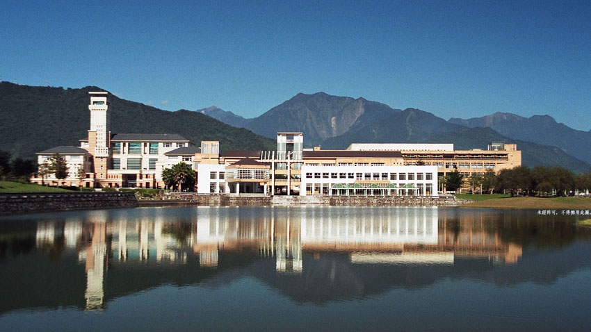 NDHU Gebäude am Wasser Ein markantes Gebäude der NDHU spiegelt sich in einem See vor einer Berglandschaft.