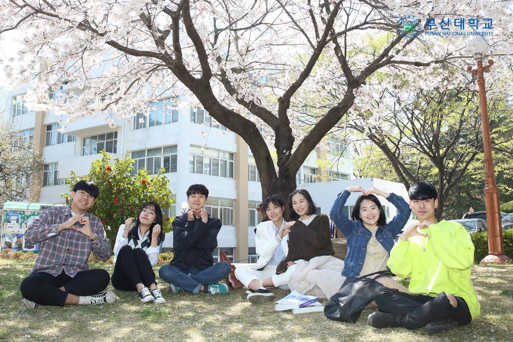 Kirschblüte an der PNU Eine Gruppe junger Menschen lächelt und posiert vor einem Gebäude der Pusan National University.