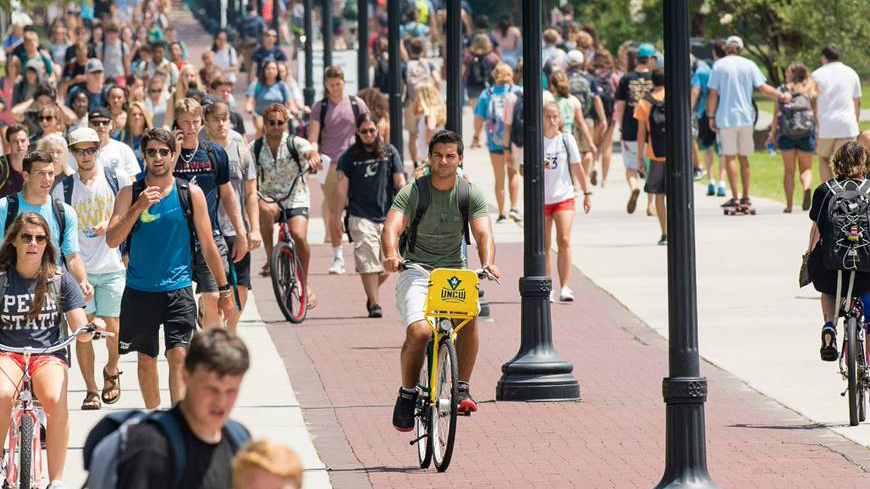 UNCW Campus Auf dem Campus UNCW. Im Vordergrund ein Studierender mit einem Fahrrad des Hawk Wheels Bike Share.