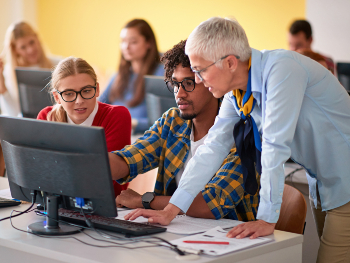 Professorin und zwei Studierende gucken gemeinsam auf Computermonitor, Professorin erläutert etwas, beantwortet Fragen o. ä. des Studenten
